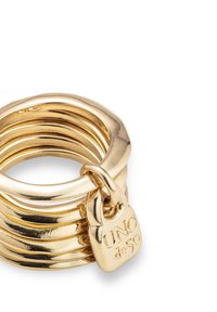 Pila de anillos de oro brillante conectados por un pequeño charm dorado grabado con "UNO de 50" sobre un fondo blanco.