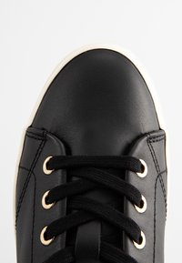 Schwarze Ledersneaker mit runder Spitze, flachen schwarzen Schnürsenkeln und goldenen Ösen. Besitzt eine crèmefarbene Gummisohle und ein glattes, strukturiertes Obermaterial.