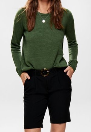 Jersey verde texturizado de manga larga combinado con pantalones cortos negros a medida, con un cinturón ancho con hebilla circular.