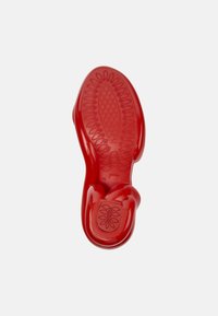 Red rubber shoe sole with textured patterns and grip detail. Curved design showing size 42, featuring a smooth, shiny finish.