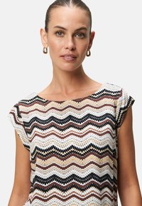 Short-sleeve top featuring a zigzag pattern in beige, brown, and black. Soft fabric with a relaxed fit and round neckline.