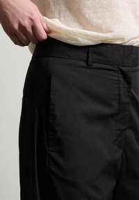 Schwarze Hose mit glatter Textur, ausgestattet mit Seitentaschen, flachem Frontdesign und klassischem Bund.
