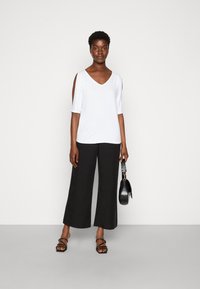 Witte top met korte mouwen en een V-hals, met uitsnijdingen op de schouders, gecombineerd met zwarte wijde broekspijpen en zwarte sandaaltjes met bandjes.