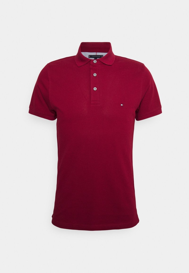 Burgundin värinen polo paita, joka on valmistettu pehmeästä kankaasta ja jossa on kolmen napin lista, lyhyet hihat ja pieni logo korostus vasemmassa rinnassa.