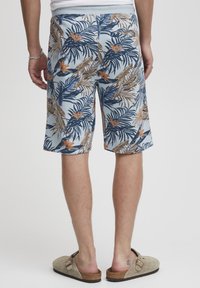 Shorts bleus à motif floral tropical comprenant des feuilles de palmier et des fleurs oranges. Fabriqués en tissu léger avec une taille élastique.