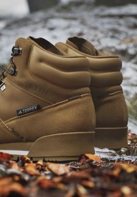 Bruine wandelschoenen met label Terrex en Cold.Rdy liggen op de grond met gevallen bladeren en lichte sneeuw.