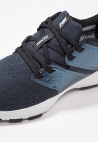 Dark blue Nike training shoe with black laces and a white sole, featuring a plastic side support panel.