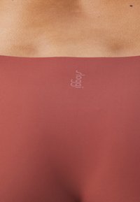 Tamno crvena bešavna sportska majica s mekim, rastezljivim materijalom; suptilan detalj s logotipom na sredini; glatka tekstura s minimalnim šavovima.