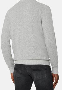 Grå stickad tröja med rundad halsringning och ribbad fåll, tillsammans med mörkgrå jeans med sömdekor på bakfickorna.