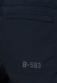 Ciemnoniebieska tkanina z teksturowanym wzorem w kratę. Posiada tylną kieszeń oraz nadrukowaną metkę "B-583" w szarym kolorze.