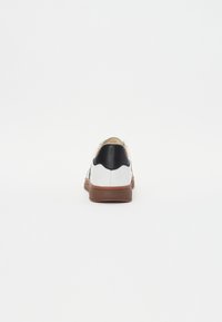White sneaker with black accents, textured sole, and smooth leather finish. Features a rounded shape and contrasting heel detail.