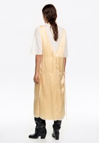 Lungo abito di raso giallo chiaro con scollatura a V profonda sul retro e lacci regolabili in vita. Abbinato a stivali neri fino al ginocchio.