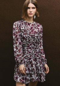 Vestido floral de manga larga, base blanca y patrones morados/negros. Presenta un corpiño ajustado y falda de volantes en capas.