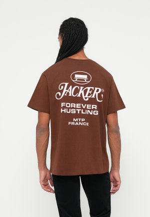 Smeđa pamučna majica s bijelim natpisima na leđima, uključujući "JACKER", "FOREVER HUSTLING" i "MTP FRANCE". Kratak rukav.