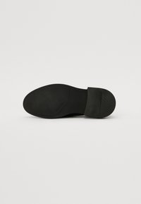 Semelle de chaussure en cuir noir avec une surface lisse, un léger talon et un motif de grip texturé. Nom de la marque embossé sur le côté.