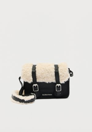 Melna rokas soma ar krēmkrāsas mākslīgās kažokādas apmali uz pārsega un plecu siksnas, divām sprādzēm un Dr. Martens logotipu priekšpusē.