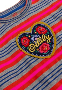 Grijze gestreepte sweater met felle roze en rode strepen. Versierd met een hartvormige geborduurde patch met kleurrijke bloemontwerpen.