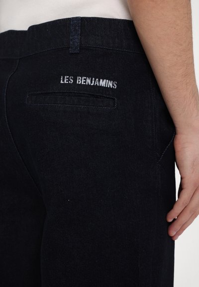 Dark denim trousers featuring embroidered "LES BENJAMINS" at the back pocket, with a sleek, straight design and minimal stitching details.