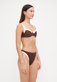 Browninga bikini komplekts ar strukturētu krūšturi ar krēmkrāsas akcentiem, priekšējo aizdari un augsto jostasvietu apakšdaļu ar atbilstošiem sānu detalizējumiem.