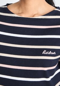 T-shirt rayé marine avec des rayures rose clair, crème et blanche. Il présente un col rond et un logo "Barbour" brodé en rose.