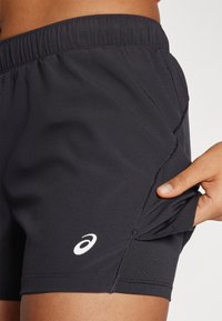 Black athletic shorts made from smooth fabric, featuring a stretchy waistband and a side pocket. Includes a white logo on the lower leg.