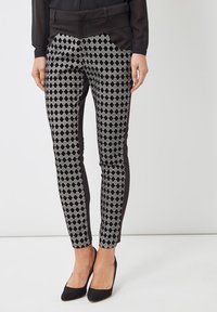 Pantalones de diseño a rayas en blanco y negro con un patrón de diamantes, textura suave, corte ajustado y una cinturilla negra sólida con paneles laterales.