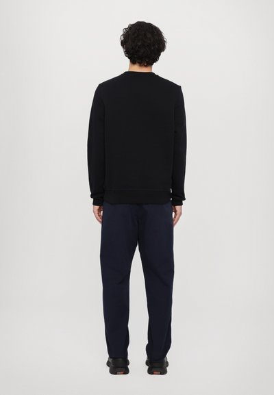 Black sweatshirt with a crew neckline and ribbed cuffs, paired with navy pants. Simple design, smooth texture, and relaxed fit.