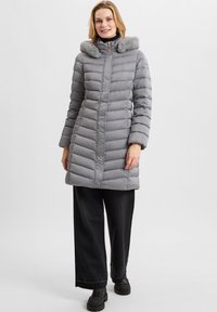 Piumino grigio con cappuccio foderato in pelliccia, design a righe verticali, chiusura con zip frontale, tasche laterali, abbinato a pantaloni neri a gamba larga e stivali.