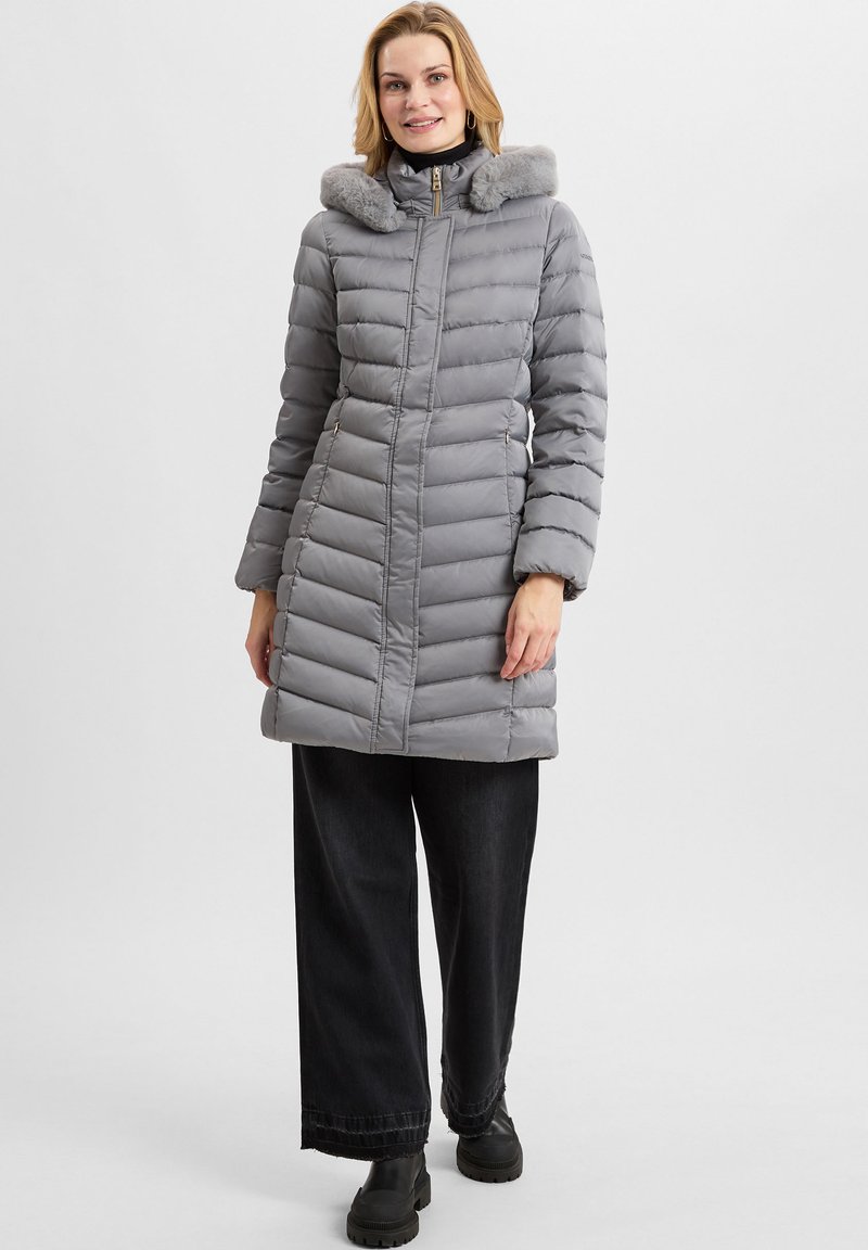 Piumino grigio con cappuccio foderato in pelliccia, design a righe verticali, chiusura con zip frontale, tasche laterali, abbinato a pantaloni neri a gamba larga e stivali.