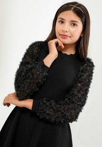 Robe noire avec un corps ajusté et des manches volumineuses en tissu texturé noir ornées d'accents floraux froncés. Détail au niveau du col à bords festonnés.