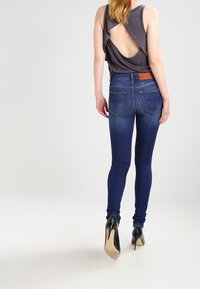 Jeans i mörk tvätt med smal passform, tillsammans med en grå ärmlös topp med ett skär i ryggen, bärs med svarta klackar.