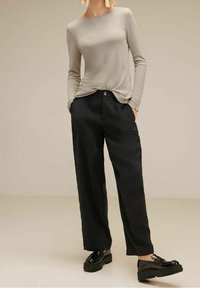 Ljust grå långärmad tröja med rundad halsringning, kombinerad med lösa svarta byxor och svarta platåskor. Slät tyg med en subtil lyster.