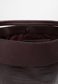 Sac à main en cuir bordeaux foncé avec une texture crocodile embossée. Intérieur spacieux avec une doublure lisse et un détail de fermeture à pression.