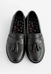 Mocasines de cuero negro con borlas de flecos, textura suave, punta redondeada y un forro interior con un patrón de corazones.