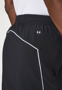 Čierne športové šortky s bielym akcentom a elastickým pásom. Obsahujú etiketu s logom Under Armour na boku. Hladká textúra tkaniny.