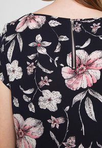Vue arrière d'un tissu bleu marine avec un grand imprimé floral rose et blanc et une fermeture éclair argentée au centre supérieur.