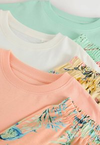 Trois hauts à col rond pliés et des shorts fleuris assortis en rose pastel, blanc et vert menthe, disposés en couches superposées.