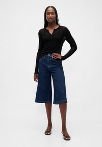 Svart ribbad långärmad topp med knäppning kombinerad med mörkblå vida jeansculottes. Har en ren fåll och hög midja.