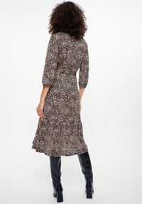 Černé a béžové šaty s leopardím vzorem, tříčtvrtečními rukávy, přiléhavým živůtkem a rozšířeným lemem, doplněné o černé kozačky po kolena.