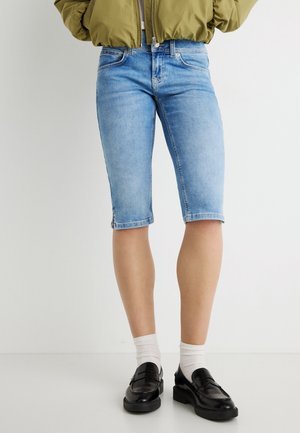 Short en jean bleu clair avec ourlet effiloché, longueur mi-cuisse, associé à des mocassins noirs et des chaussettes blanches. Comprend un design classique à cinq poches.