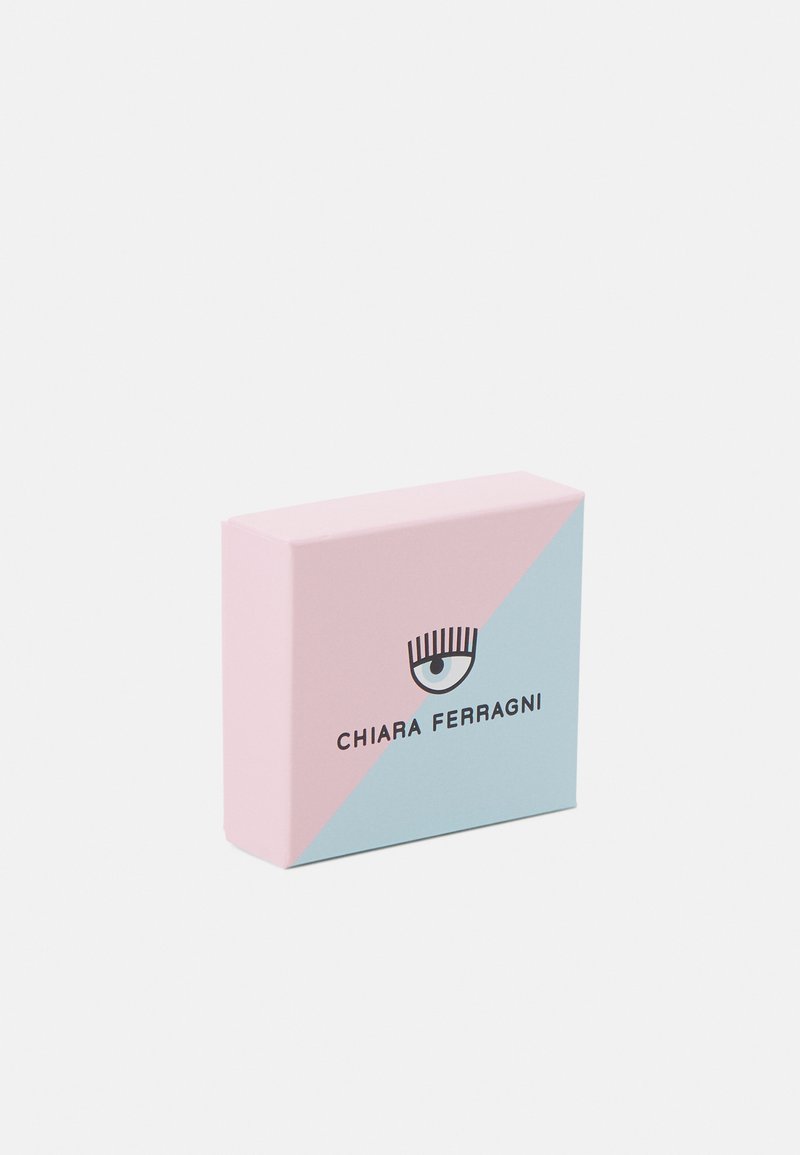 Boîte carrée avec un design géométrique rose et bleu clair, comportant un logo d'œil noir et le texte "CHIARA FERRAGNI" en caractères gras.