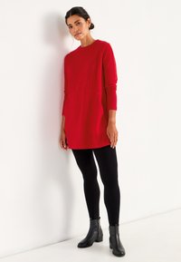Rode gebreide tuniek met lange mouwen en een ronde halslijn, gecombineerd met zwarte leggings en enkellaarsjes. Heeft een Relaxed fit en zakken.