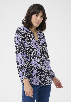 Blusa a maniche lunghe di un blu navy scuro con un pattern a stampa leopardata colorato in viola, bianco e grigio. Caratterizzata da un colletto a V e una vestibilità ampia.