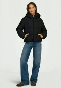 Μαύρο μπουφάν puffer με στενή κουκούλα, μπροστινό φερμουάρ και δύο πλαϊνές τσέπες. Φοριέται με μπλε τζιν και καφέ μποτάκια μέχρι τον αστράγαλο.