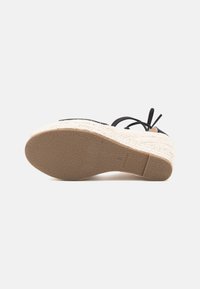 Wedge-Espadrille-Sandale mit beiger geflochtener Jutesohle, strukturiertem braunem Gummi-Außensohle und schwarzen Knöchelriemen, von der Sohle aus dargestellt.