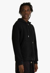 Felpa nera con zip, realizzata in materiale in pile, con tasca frontale, cappuccio con coulisse e dettagli con zip color argento.