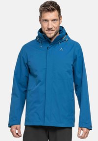Chaqueta impermeable azul con capucha, hecha de tejido suave. Presenta un cierre de cremallera frontal, cordones ajustables y dos bolsillos laterales.