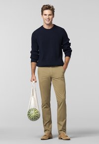 Marineblå ribbet crew neck sweater, beige chinos og beige loafers. Holder en mesh tote med grønne bolde. Enkel design, afslappet pasform, neutrale farver.