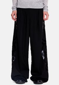 Plačios juodos medžiagos kelnės su blizgiomis juodomis šoninėmis detalėmis. Elastinga liemens juosta ir laisvas kirpimas užtikrina komfortą.