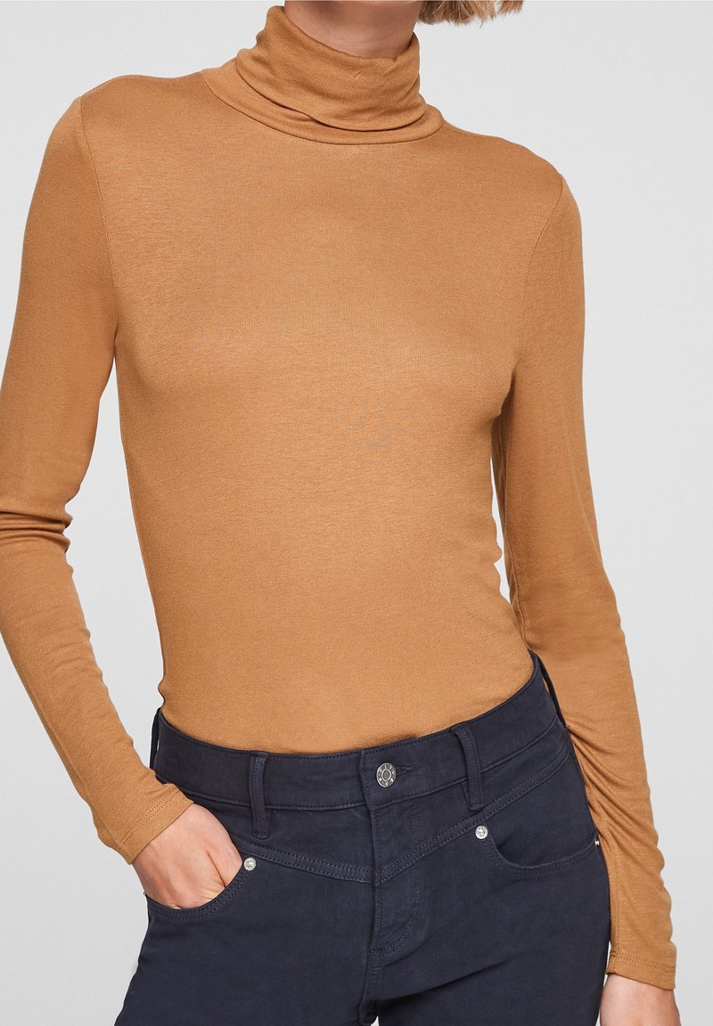 Lichtgewicht, gladde bruine turtleneck top met lange mouwen. Heeft een getailleerde snit en is gecombineerd met marineblauwe broek.